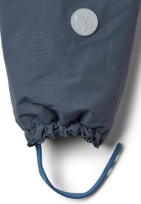 Sininen kangastuote, jossa on rypytetty aukko, pyöreä harmaa logokyltti ja joustava sininen hihna pohjassa.