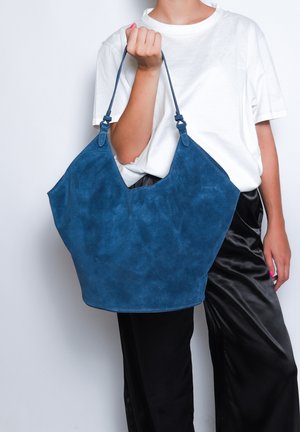 Blauwe suède handtas met een brede, open top, V-vormige opening en twee korte schouderbanden. Zachte textuur en gestructureerde vorm.