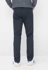 Donkerblauwe, gestructureerde broek met een recht model, voorzien van twee achterzakken, gedragen met witte en blauwe sneakers.