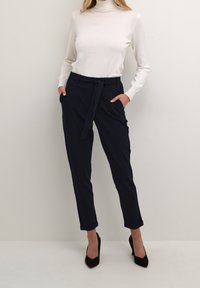 Pantalons marine à coupe décontractée, taille haute et ourlets retroussés. Associés à un pull col roulé crème et des chaussures à talons hauts noires.