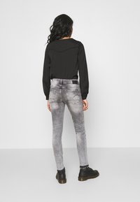 Top negro de manga larga con cuello redondo, acompañado de unos jeans ajustados de mezclilla gris, con un diseño desvanecido y bolsillos traseros. Botas negras completan el look.