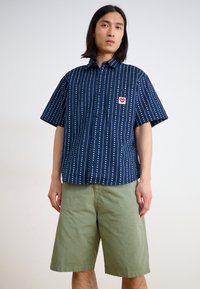 Short-sleeve navy shirt with vertical white stripes, and a small red heart patch on the chest, paired with light green shorts.