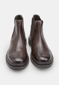 Stivaletti in pelle marrone con pannelli laterali elastici, punta tonda e suola piatta, caratterizzati da una texture liscia e un design minimal.