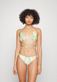Conjunto de bikini com um top triangular e parte de baixo de cintura baixa em branco, com padrões de limões amarelos e folhas verdes, alças ajustáveis e detalhes listrados.