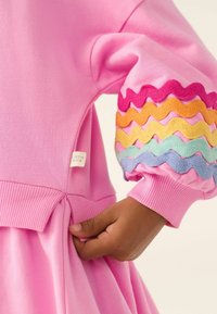 Rosa Kleid mit gerippten Bündchen und mehrfarbigem Wellen-Stickerei. Seitenetikett mit der Aufschrift "Little Bird." Weicher, strukturierter Stoff.