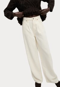 Pantaloni bianchi a gamba larga realizzati in tessuto morbido, con vita alta, pieghe e dettagli di cucitura sottili. Abbinati a un maglione di maglia scuro.
