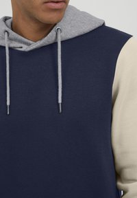 Sudadera con capucha de color azul marino, con capucha gris y mangas de color crema. Tejido suave con cordones y ojales para ajuste.