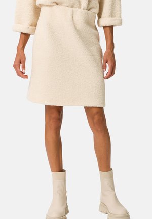Jupe texturée fluffy de couleur crème avec une taille ajustée, atteignant mi-thigh, associée à des bottines beiges. Surface lisse, design décontracté.