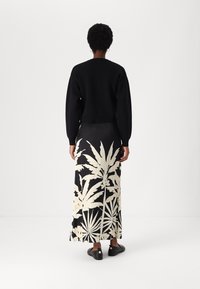 Zwarte cropped sweater gecombineerd met een lange zwarte rok met een groot wit bladpatroon. Model draagt zwarte instapschoenen met accenten.