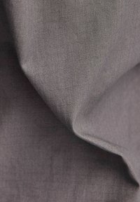 Šedá strukturovaná tkanina s jemným mřížkovým vzorem, vykazující měkké záhyby a hladký povrch. Materiál se zdá být lehký a univerzální.