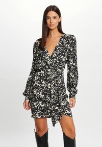 Abito floreale stampato in bianco e nero con maniche lunghe, scollatura a V, vita cinchata e design avvolgente, abbinato a stivali neri al ginocchio.