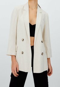 Beige dvouřadý blazer vyrobený z lnu s volným střihem. Ozdobený velkými kovovými knoflíky a klopami, kombinovaný s černým topem.