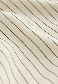Tissu blanc avec de fines rayures noires verticales, légèrement froissé et texturé.