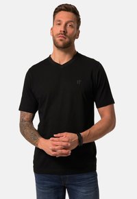 Sort kortærmet V-hals T-shirt med et diskret logo på brystet, lavet af et glat stof. Modellen bærer blå jeans og har hænderne foldet.