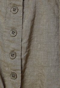 Koszula zapinana na guziki w oliwkowym lnie. Posiada cztery ciemne guziki z przodu, teksturowany materiał o delikatnym połysku.