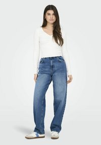 Witte lange mouwen top gecombineerd met high-waisted, losse blauwe denim jeans en witte sneakers met blauwe strepen en een beige zool.