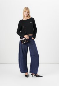 Black cropped sweater with "GAP" logo, paired with wide-leg blue jeans featuring stitching details, and black pointed heel shoes. Brown crossbody bag.