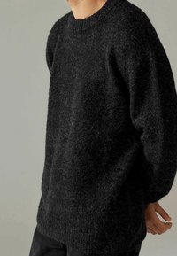 Maglione nero in maglia spessa con scollatura rotonda e maniche lunghe, caratterizzato da un tessuto testurizzato e soffice e orlo a coste nella parte inferiore.