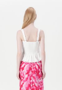 Hvit peplum topp med justerbare stropper og smocket rygg, båret over et rosa blomstertrykt skjørt med en myk, flytende tekstur.
