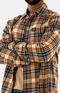 Camisa de franela a cuadros en crema, azul marino y burdeos. Presenta un cierre de botones al frente, bolsillo en el pecho y un ajuste relajado con mangas arremangadas.