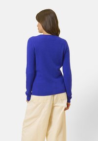 Maglione a maglia blu royal, aderente, con maniche lunghe e scollatura rotonda, abbinato a pantaloni beige chiaro a gamba larga. Morbido al tatto con polsini a costine.