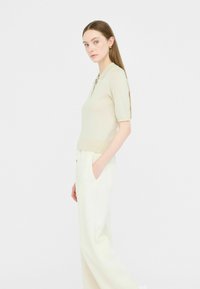Polo top lavorato a maglia in beige chiaro, con maniche corte, colletto e finitura testurizzata. Abbinato a pantaloni bianchi a vita alta e gamba larga.