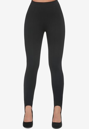Czarne legginsy z wysokim stanem o gładkiej, gładkiej fakturze i detalach szwów, w zestawieniu z czarnymi butami na wysokim obcasie.