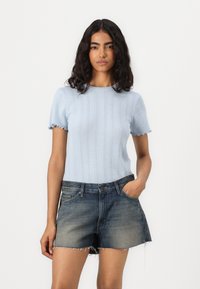 Lichtblauw geribbeld gebreid T-shirt met gekartelde mouwen, gecombineerd met donkere denimshorts met een rafelige zoom en een klassiek vijf-pocket ontwerp.