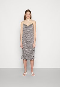 Vestido slip em preto e branco com bolinhas, com alças finas, apresentando um decote em V e uma silhueta reta, atingindo a altura da metade da panturrilha.