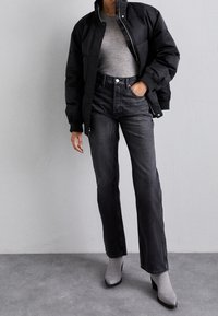 Giacca piumino nera, top grigio a coste, jeans neri a vita alta e stivaletti grigi con tacco. Texture lisce e silhouette aderente.