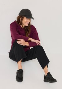 Burgundi kapuutsiga sviiter, must kork, mustad laiad teksapüksid ja mustad tossud. Sile kangas, millel on peen läige ja tekstuuriga jalanõud.