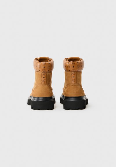Tan suede ankle boots with a patterned leather cuff, chunky black sole, and reinforced stitching on the back for durability.