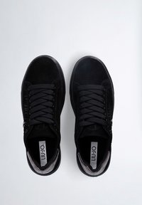 Black suede sneakers with a smooth texture, rounded toe, and flat laces. Featuring a metal zipper accent and logo on the tongue.