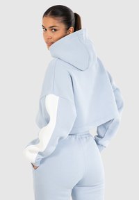Sudadera corta de color azul claro con mangas oversize, detalles en blanco y capucha con cordón, combinada con pantalones de cintura alta a juego.