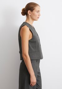 Gray pinstriped cropped vest with a V-neck, sleeveless design, five buttons, and side pockets. Smooth texture, tailored fit.