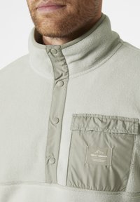 Lichtgroene fleece pullover met een halve ritssluiting, drukknoopjes en een borstzak met een logo en stofaccentdetails.