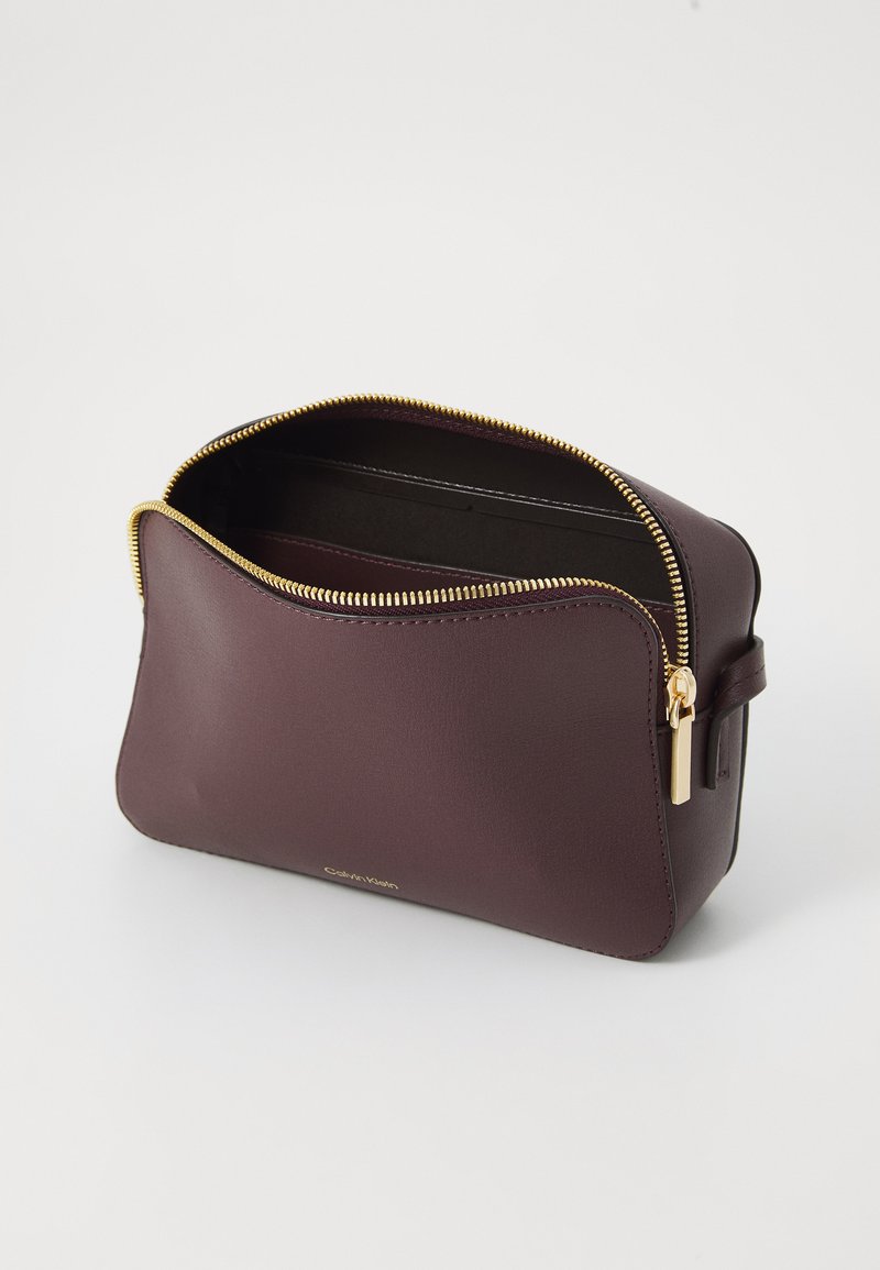 Borsa per trucchi in pelle bordeaux con zip dorata, leggermente aperta per rivelare l'interno, caratterizzata da un design minimalista e una maniglia laterale.