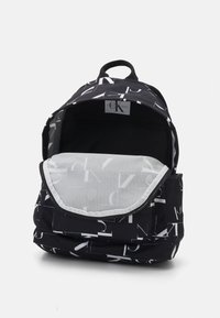 Zaino nero con motivo del logo bianco di Calvin Klein, chiusura con zip, materiale in tessuto e un ampio scomparto principale con una morbida fodera interna.