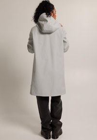 Light gray waterproof coat with a hood, long sleeves, and a straight cut, paired with dark gray pants and black shoes.