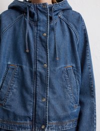 Jeansjacke mit Kapuze in blauer Farbe, mit silbernen Druckknöpfen, verstellbaren Kordeln und Fronttaschen mit orangefarbenen Nähten.