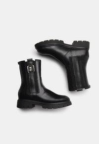 Schwarze Lederknöchelstiefel mit chunky Sohle, seitlichem Reißverschluss und vertikalen Streifenakzenten. Glatte Textur und robuste Konstruktion.