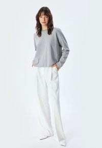 Maglione grigio chiaro a maglia con scollatura a girocollo e spalle cadenti, abbinato a pantaloni bianchi a vita alta con gamba larga e scarpe con punta.