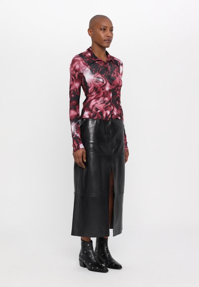 Enganliegende Bluse mit langen Ärmeln in pink und dunkelrot floralem Muster, kombiniert mit einem schwarzen Lederrock mit einem Schlitz vorne und schwarzen hohen Stiefeln.
