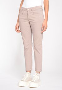 Ljust beige, åtsittande jeans med en slät textur, fem fickor och knäppning med knapp. Stylerade med vita högskaftade sneakers.