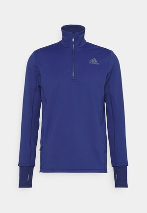 Sudadera azul de manga larga de Adidas con cremallera hasta un cuarto, orificios para el pulgar en los puños y logo de Adidas en el pecho sobre fondo blanco.