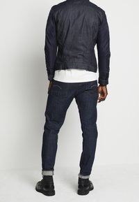 Mörk denimjacka med ett slätt marinblått tyg, figursydd stil och ribbade ärmar. Matchas med mörkblå jeans och svarta ankelstövlar.