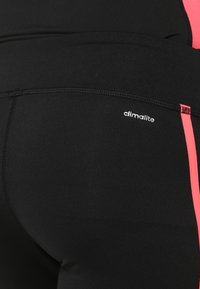 Black athletic leggings with pink side stripes and "climalite" logo on the back right hip.
