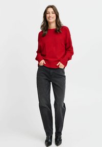 Rode gebreide trui met ribbelboorden en onderkant, gecombineerd met zwarte high-waisted jeans en zwarte puntige enkellaarsjes. Eenvoudige, casual pasvorm.