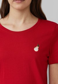 Rode katoenen T-shirt met een ronde halslijn. Heeft een kleine geborduurde aardbei in het wit en groen op de linker borst.