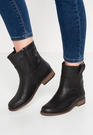 Sorte læderankelstøvler med sidelås og brun sål, båret med blå skinny jeans rullet let op over anklen.
